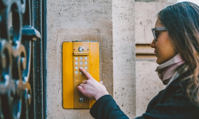 Woman at an exterior door entering a code on the keypad of a vibrant yellow intercom.