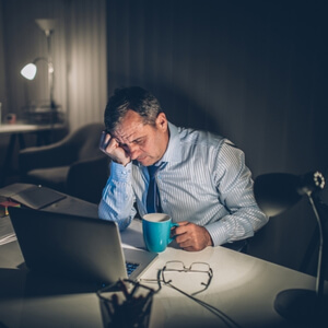 tired man at the computer at night holding his head and a cup of coffee
